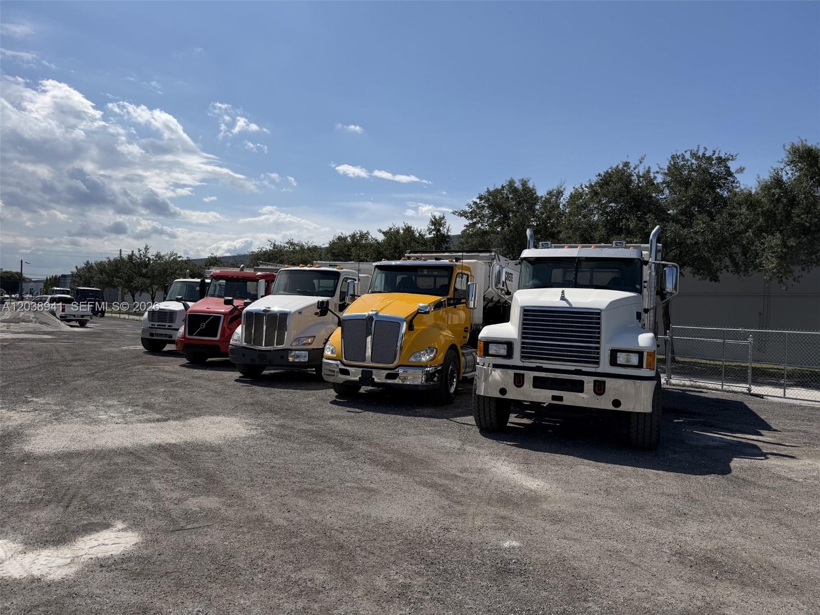 A row of five commercial dump trucks is parked on a gravel lot — MEDLEY, FL