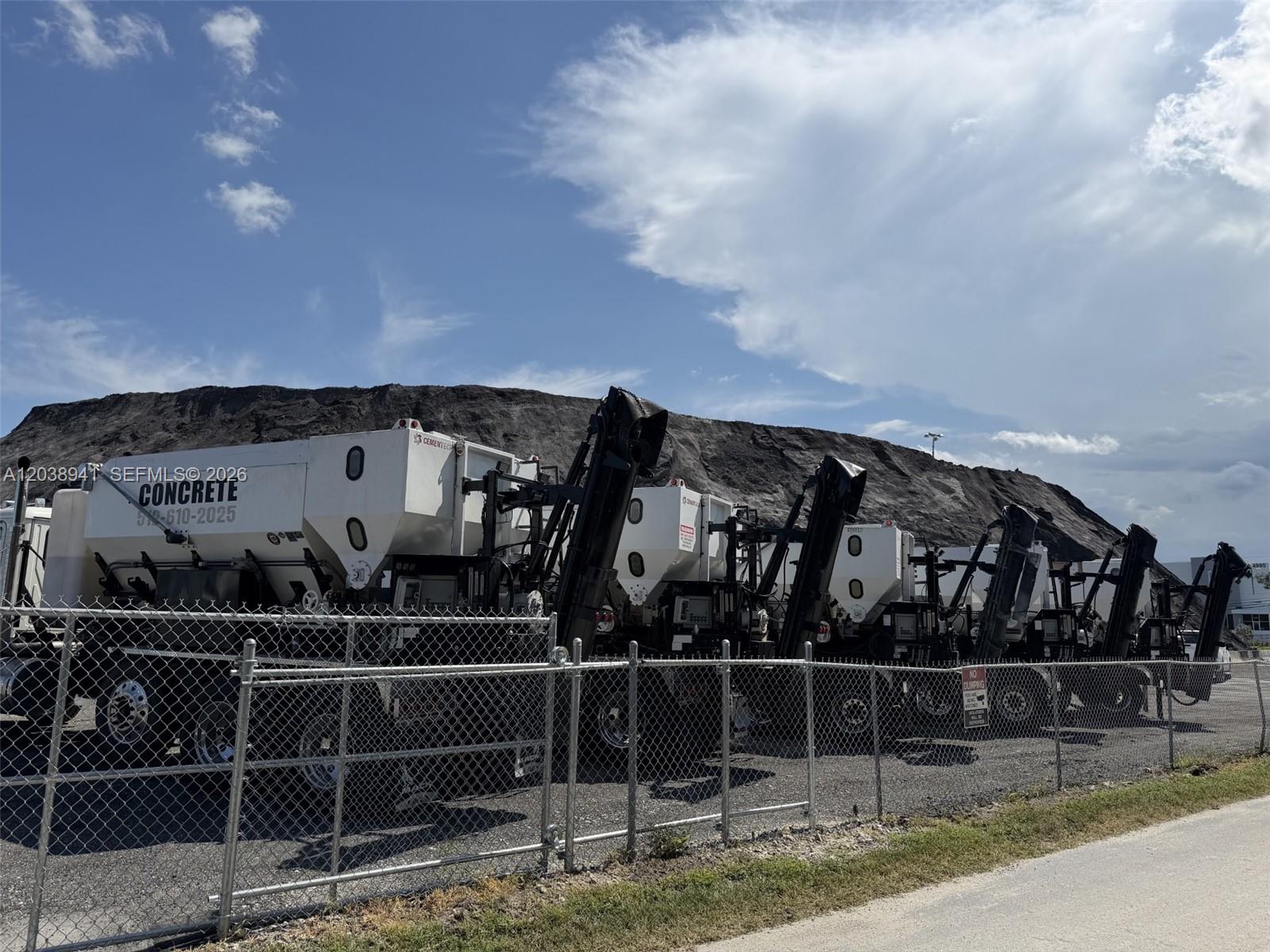 A row of white concrete mixer trucks is parked behind a chain-link fence — MEDLEY, FL