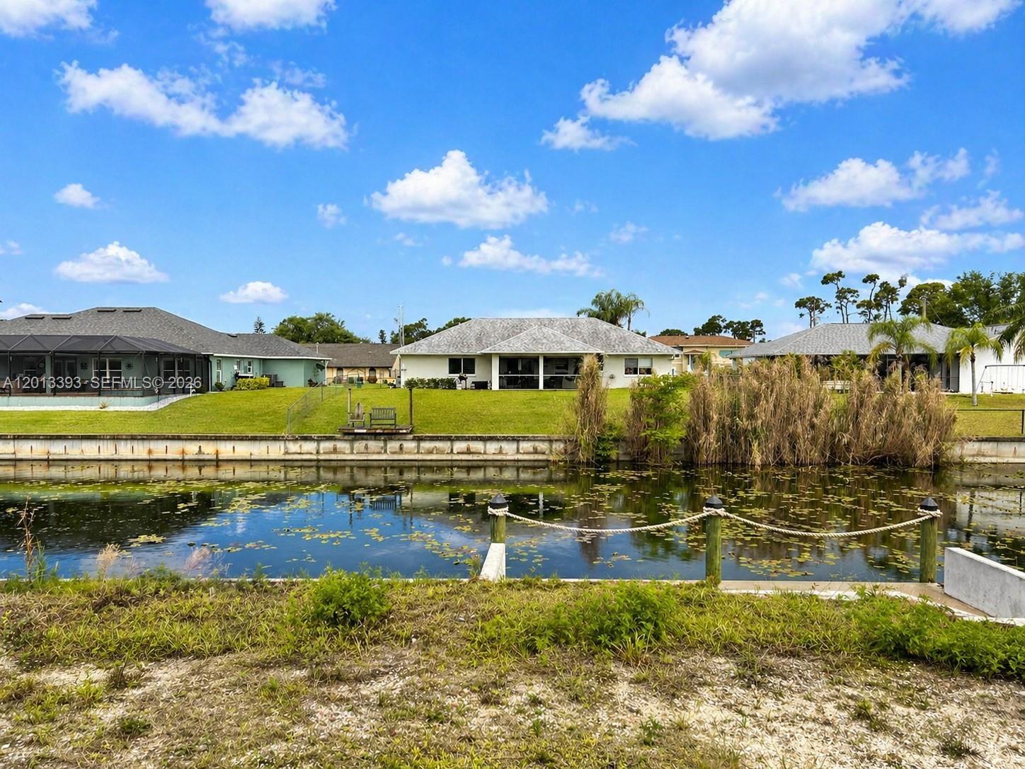 A canal separates a grassy backyard with houses from the foreground — 1014 SW 18th St, Cape Coral FL 33991, CAPE CORAL, FL