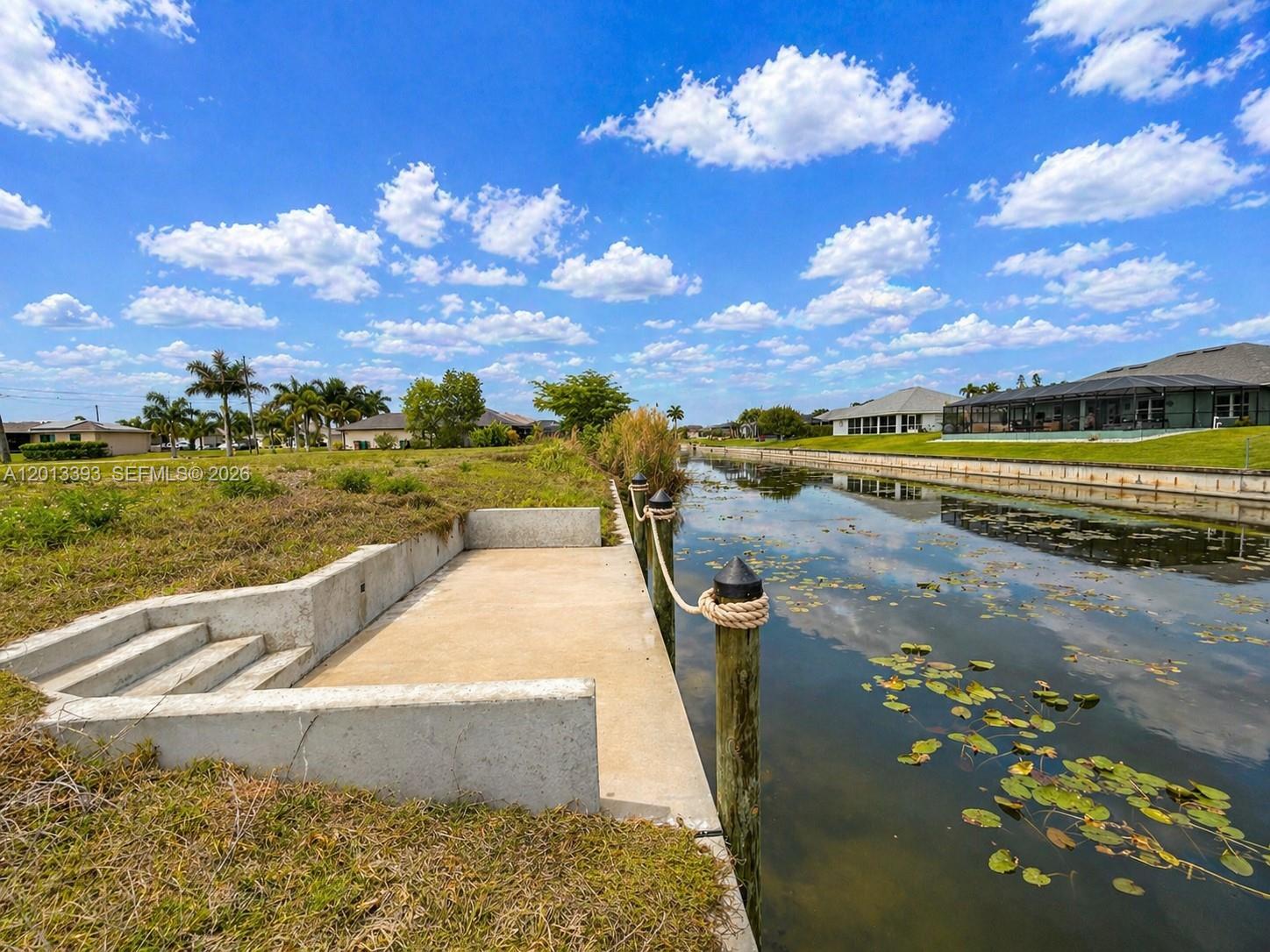 A concrete dock with wooden pilings sits along a canal behind a grassy yard — 1014 SW 18th St, Cape Coral FL 33991, CAPE CORAL, FL