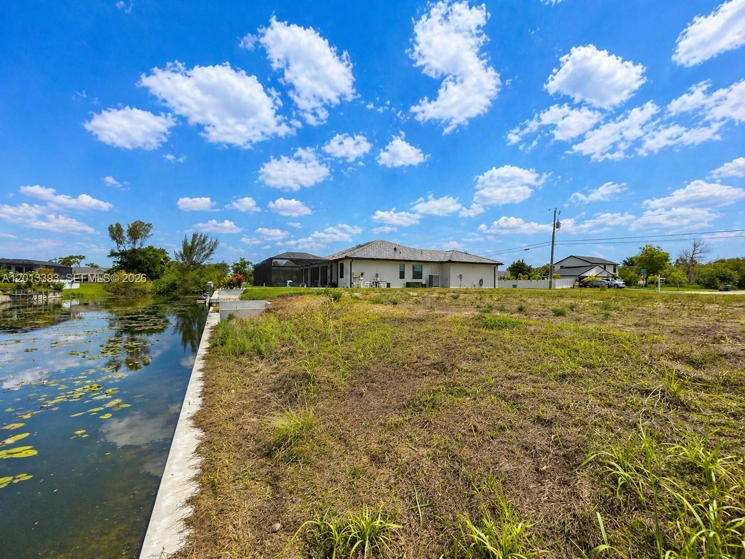 A view of a grassy lot bordering a canal with a house in the background — 1014 SW 18th St, Cape Coral FL 33991, CAPE CORAL, FL
