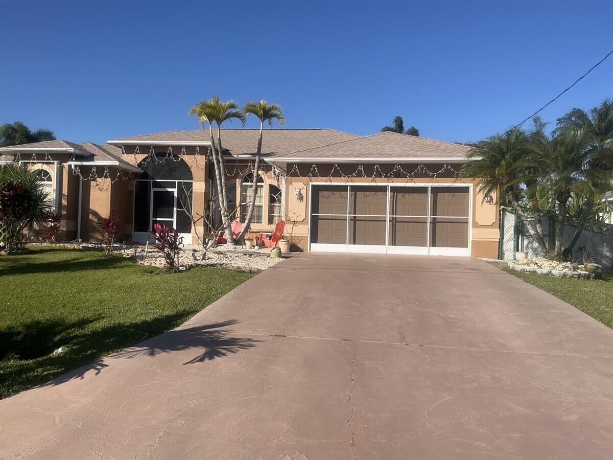 A single-story house with a tan stucco exterior, a screened garage, and palm trees — 5640 NW Commodore Terrace, Port St. Lucie FL 34983, PORT ST. LUCIE, FL