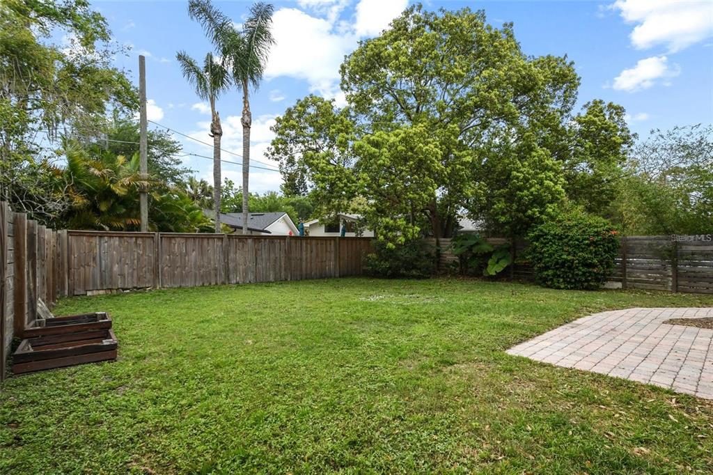 A grassy backyard features a wooden fence, a brick patio, and several large trees — 1627 ORANGE AVENUE, WINTER PARK, FL