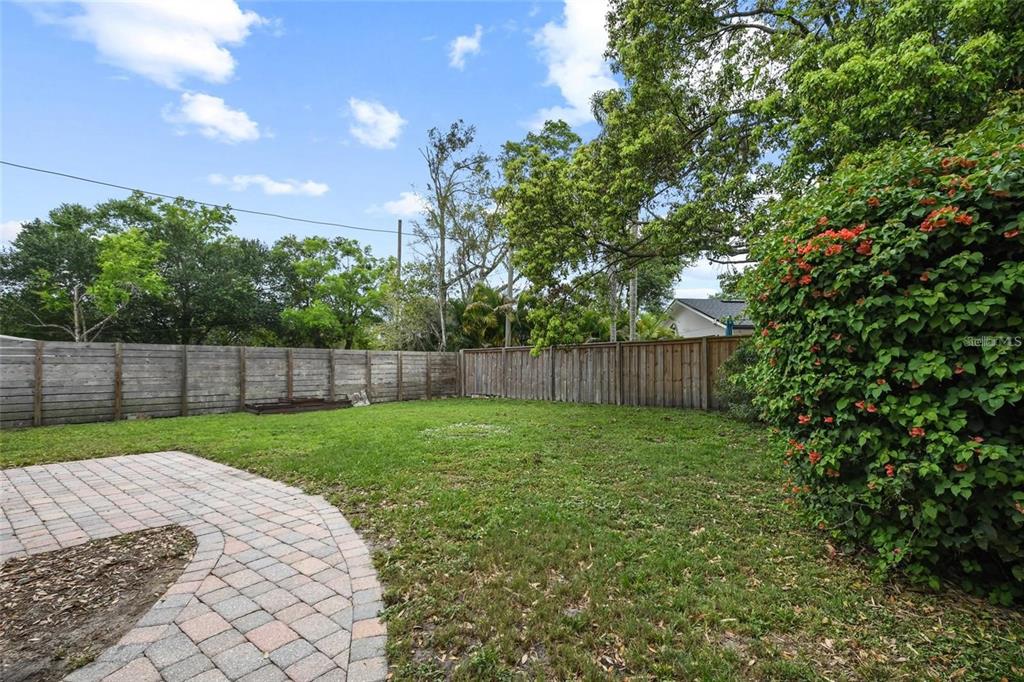 A backyard features a paved stone walkway, a grassy lawn, and a wooden privacy fence — 1627 ORANGE AVENUE, WINTER PARK, FL