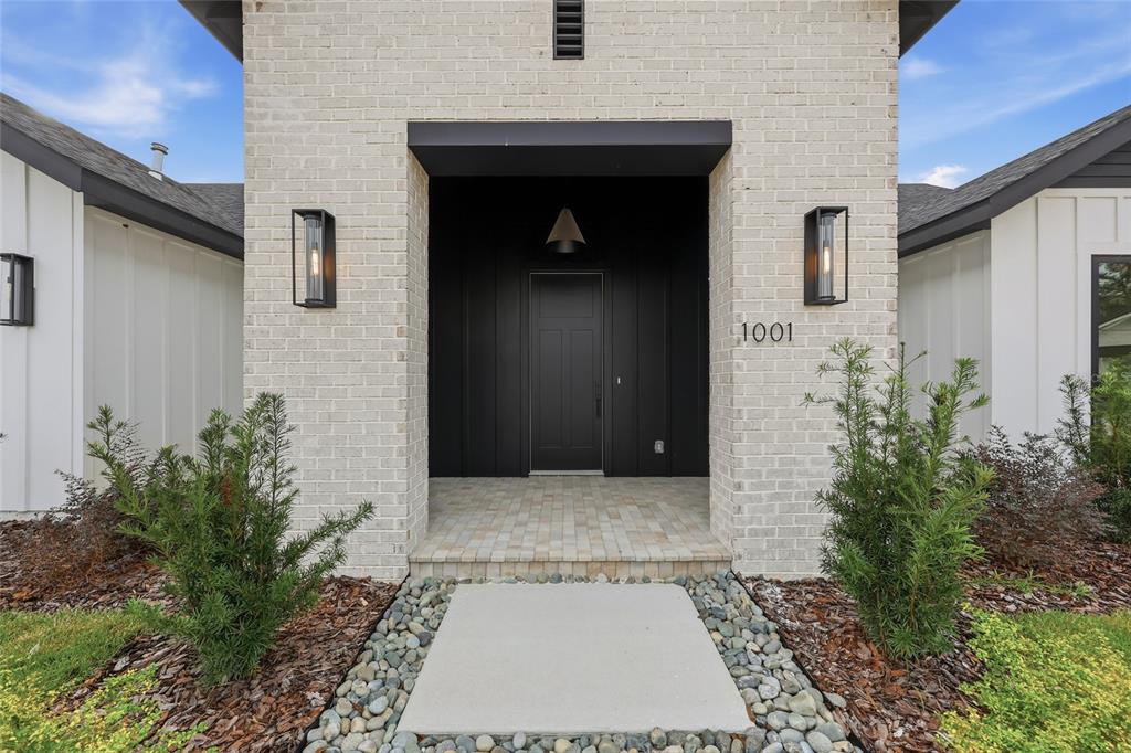 The exterior of a modern house features a brick facade, black door, and two lanterns — 1001 SW 120TH DRIVE, GAINESVILLE, FL