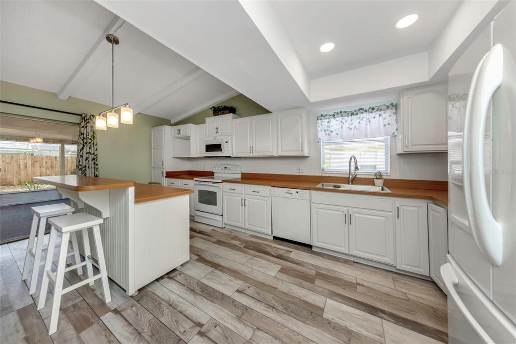 A kitchen with white cabinets, wood countertops, a breakfast bar, and wood-look tile flooring — 17704 RIVENDEL ROAD, LUTZ, FL