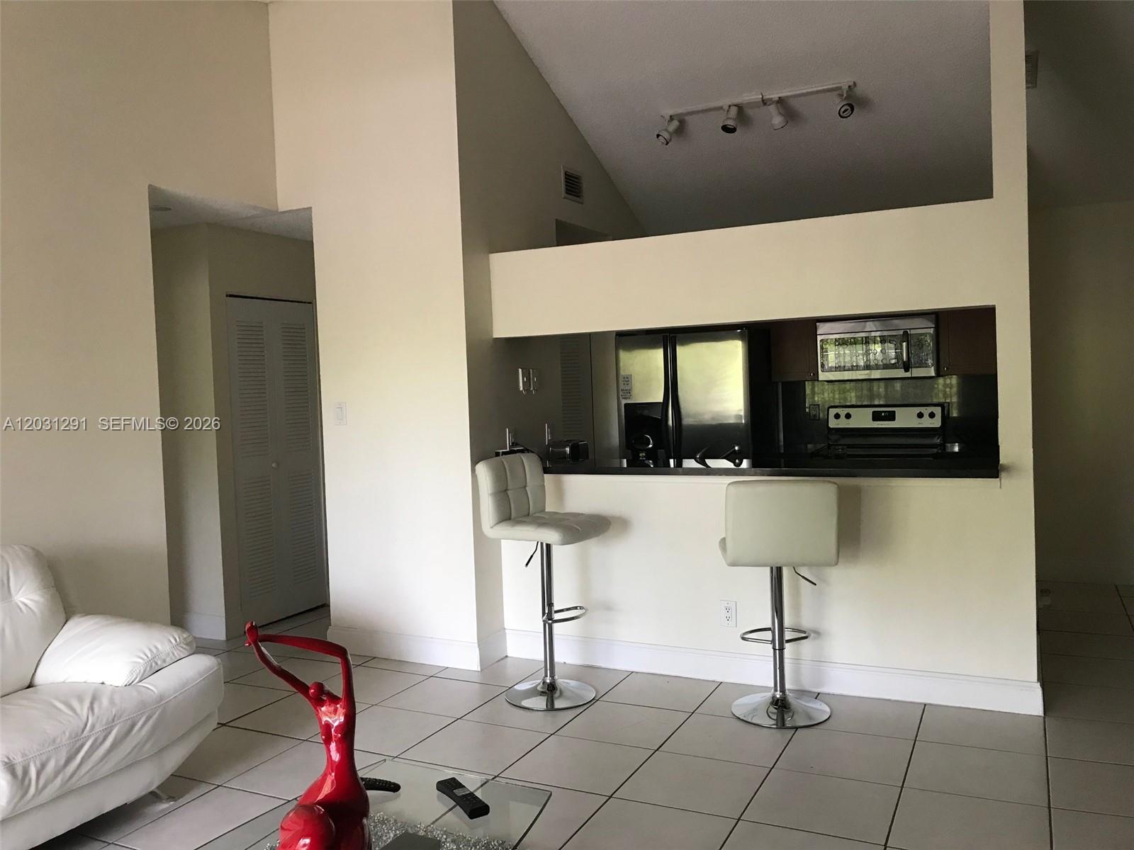 A living room features white tile floors, a white sofa, and a kitchen breakfast bar — 10610 SW 158th Ct # 303, Miami FL 33196, MIAMI, FL