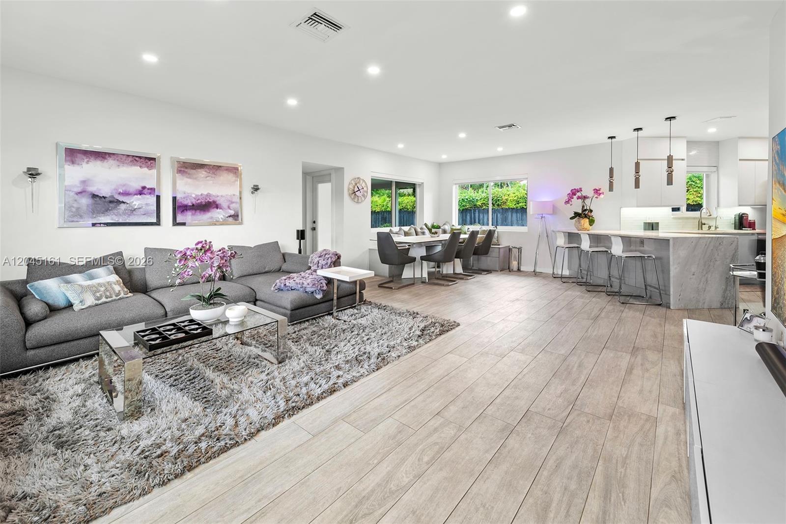 A modern open-concept living room features a gray sectional, dining area, and kitchen island — 1724 71st St, Miami Beach FL 33141, MIAMI BEACH, FL
