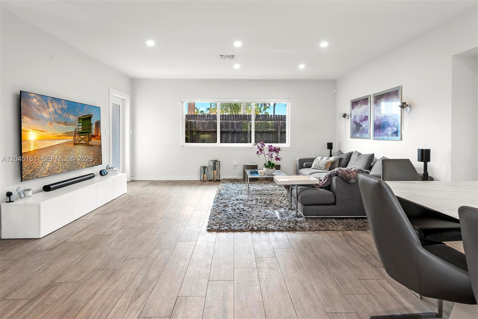 A modern living room features wood-look tile flooring, a large television, and a gray sectional — 1724 71st St, Miami Beach FL 33141, MIAMI BEACH, FL