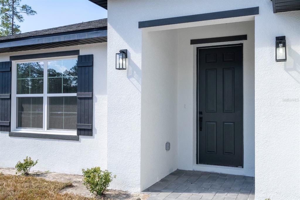A white stucco house exterior features a black front door, matching shutters, and outdoor lighting — 3803 BREWSTER ROAD, NORTH PORT, FL