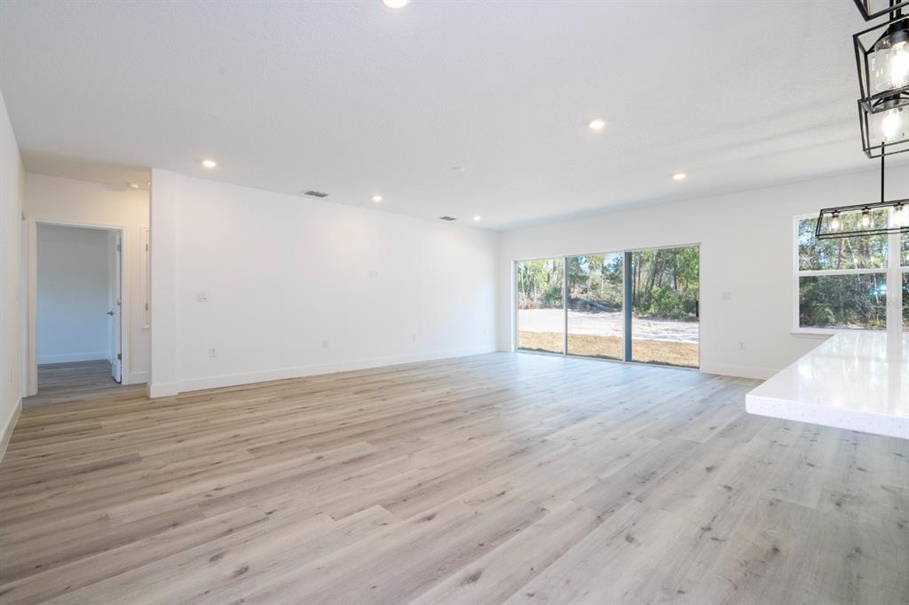 An open-concept living area features light wood-look flooring, white walls, and large sliding glass doors — 3803 BREWSTER ROAD, NORTH PORT, FL
