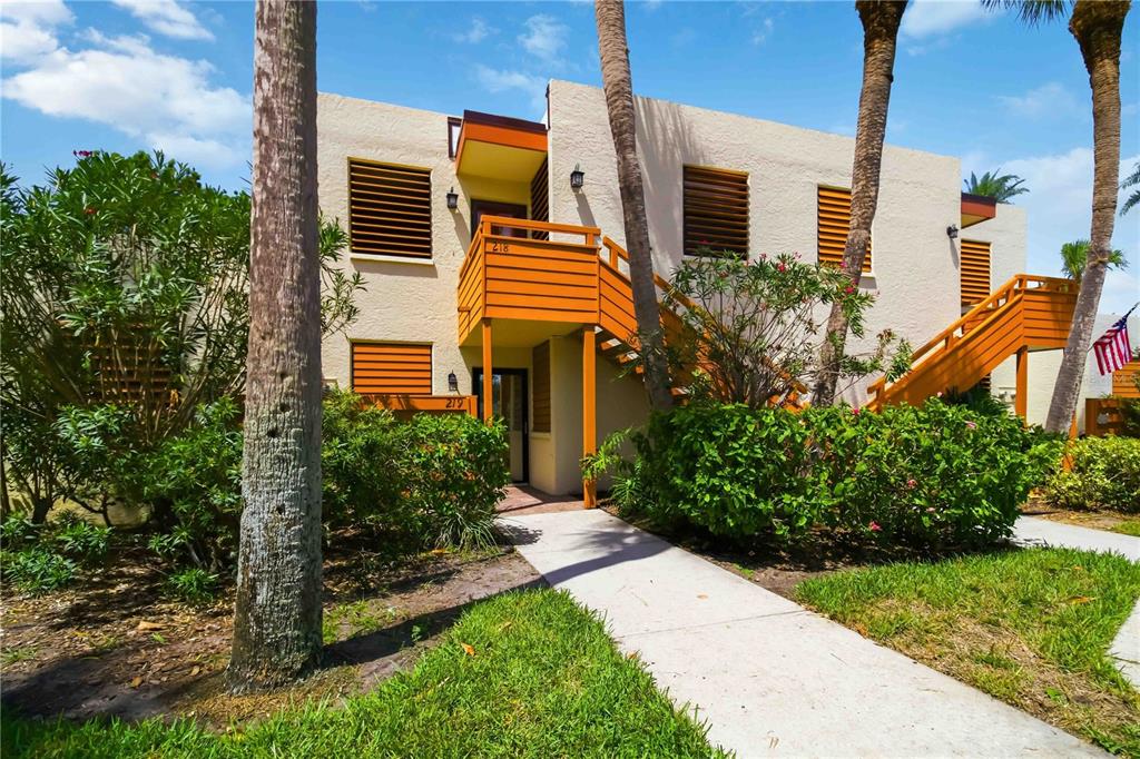 A two-story tan building features orange wooden staircases and balconies surrounded by palm trees — 218 PINENEEDLE DRIVE UNIT 218, BRADENTON, FL