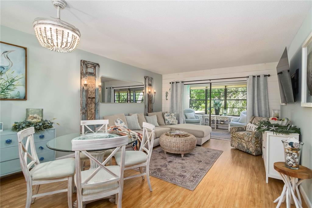 A coastal-style living and dining room features light wood floors, a sectional, and glass doors — 218 PINENEEDLE DRIVE UNIT 218, BRADENTON, FL