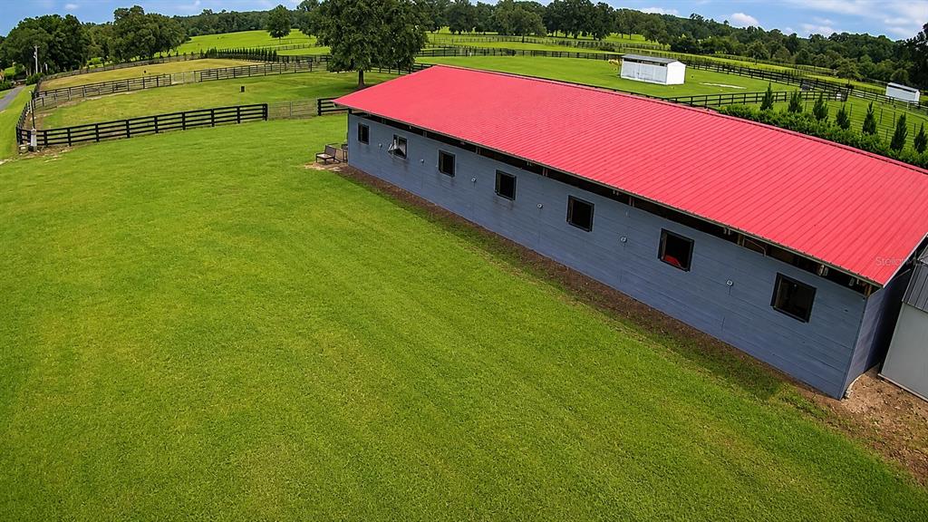 An aerial view shows a long, grey horse barn with a red metal roof — 8020 NW 115TH AVENUE, OCALA, FL