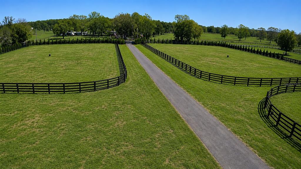 An aerial view shows a paved driveway flanked by fenced pastures and mature trees — 8020 NW 115TH AVENUE, OCALA, FL