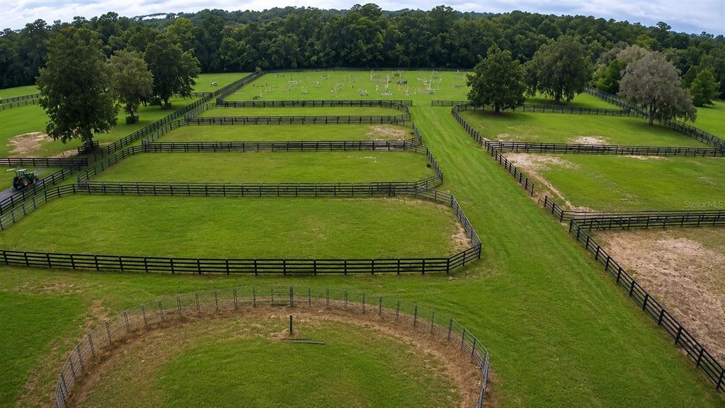 An aerial view shows multiple fenced horse paddocks and a round pen on a grassy property — 8020 NW 115TH AVENUE, OCALA, FL