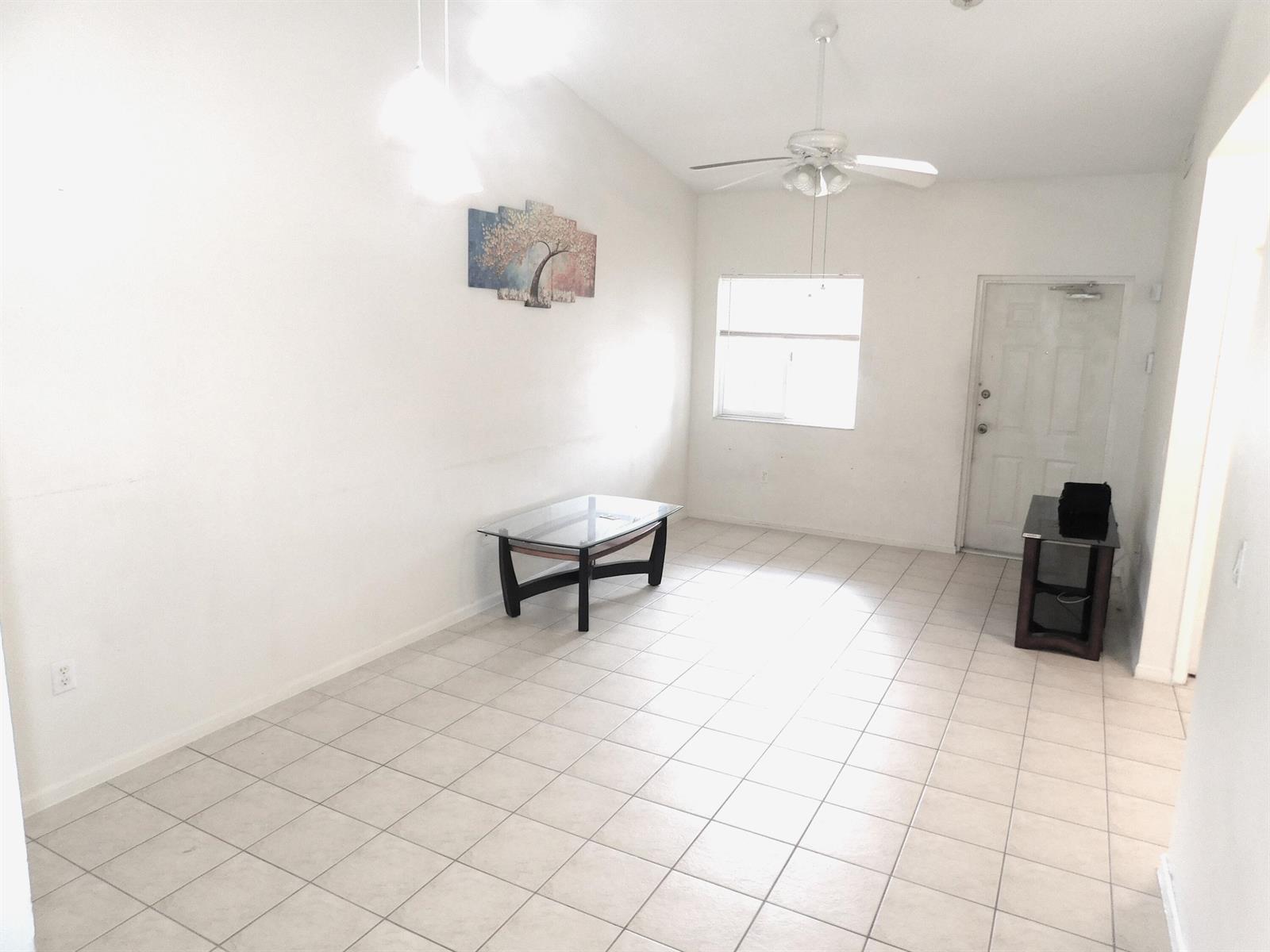 An empty living room features white walls, light tile flooring, a ceiling fan, and windows — 3800 N Jog Road # 204, West Palm Beach FL 33411, WEST PALM BEACH, FL