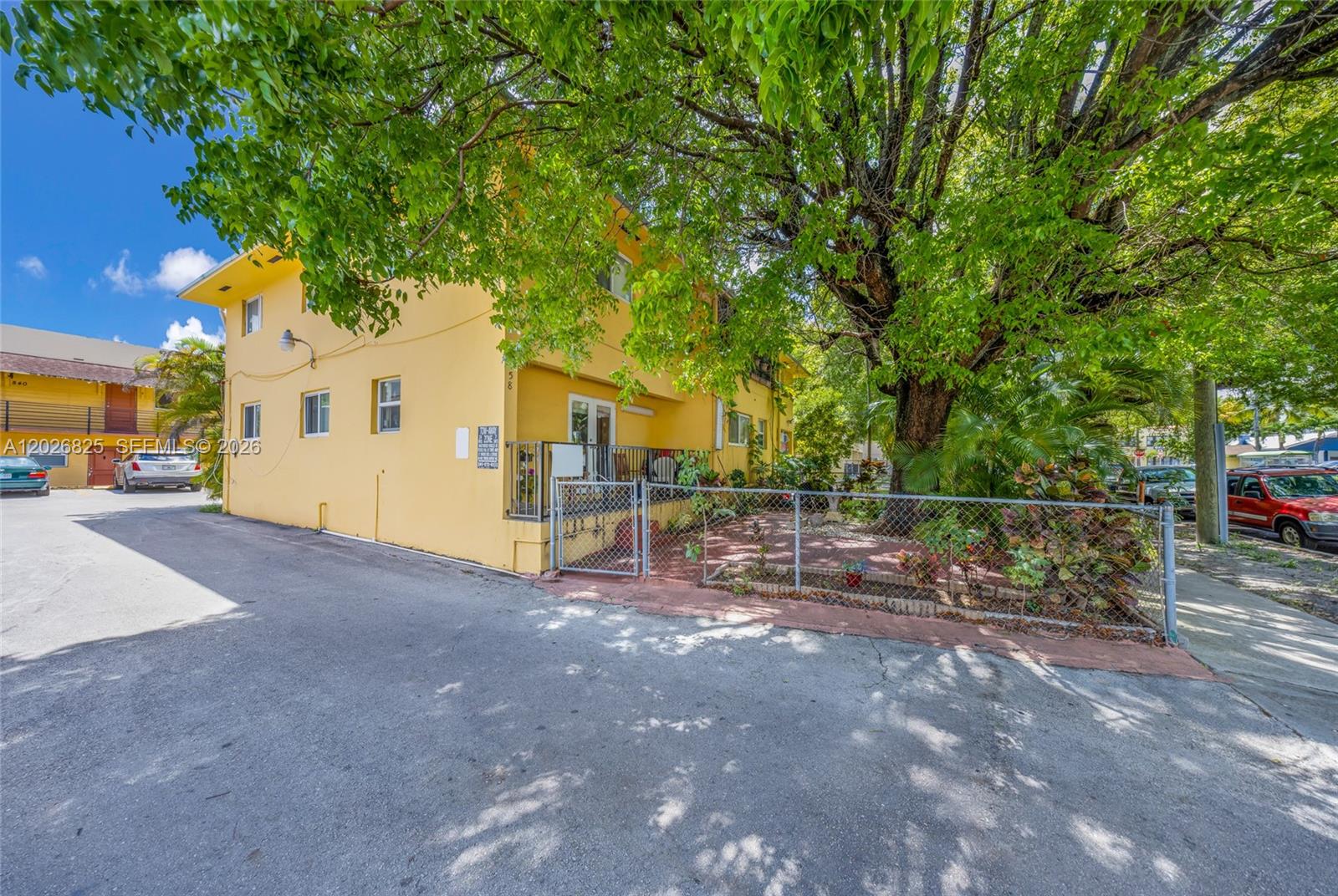 A yellow two-story building features a fenced-in patio area shaded by a large tree — 840 NW 4th St, Miami FL 33128, MIAMI, FL