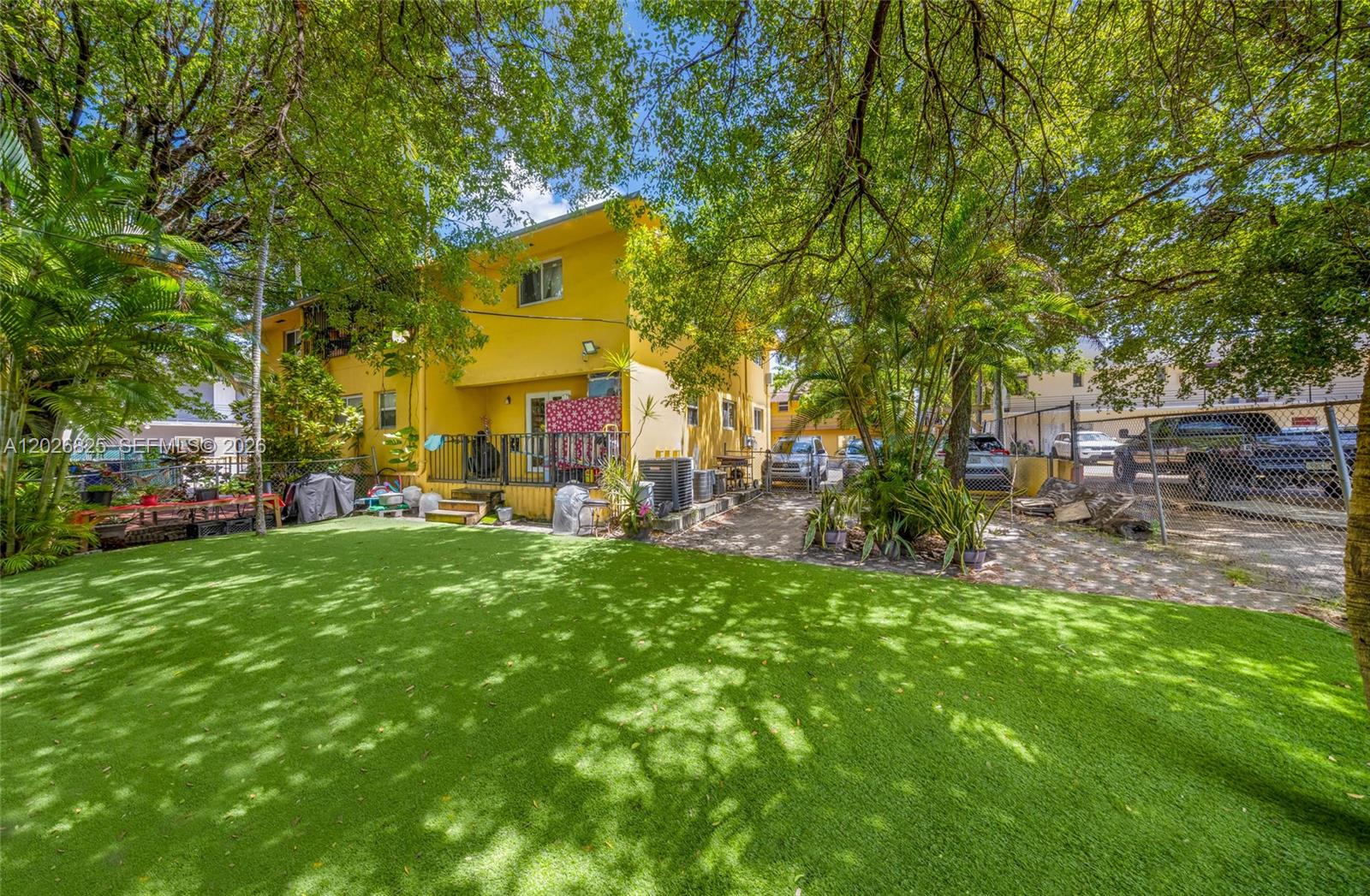 A yellow two-story building features a backyard with artificial turf and mature trees — 840 NW 4th St, Miami FL 33128, MIAMI, FL