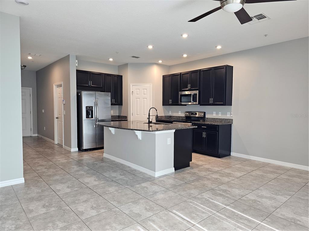 A kitchen with dark cabinets, granite countertops, a center island, and light tile flooring — 10548 SALT GROVE ST, ORLANDO, FL