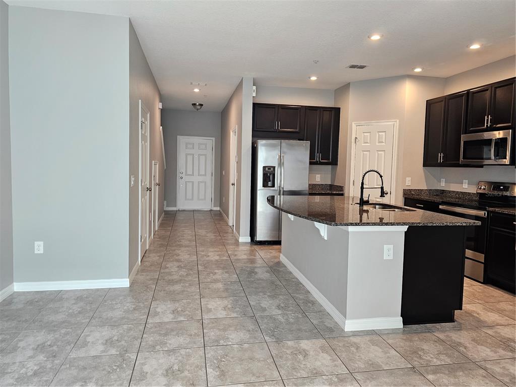 A kitchen with dark cabinets, granite countertops, and a breakfast bar overlooks a tiled hallway — 10548 SALT GROVE ST, ORLANDO, FL