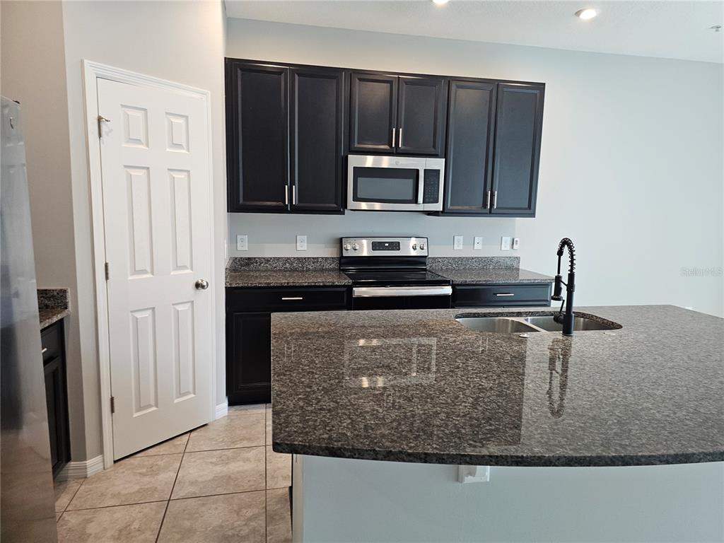 A kitchen features dark cabinets, granite countertops, stainless steel appliances, and a large island — 10548 SALT GROVE ST, ORLANDO, FL