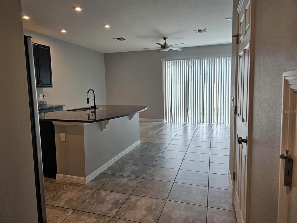 A kitchen with a dark granite island and tile flooring opens into a living area — 10548 SALT GROVE ST, ORLANDO, FL