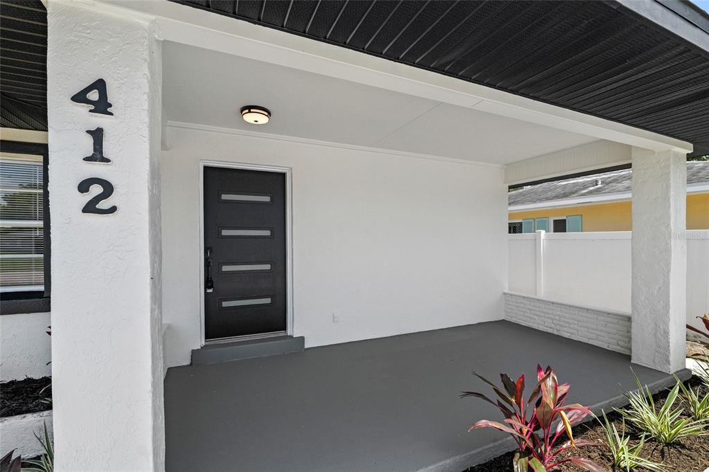 A covered front porch features a dark gray door, white walls, and a painted floor — 412 20TH AVENUE W, PALMETTO, FL