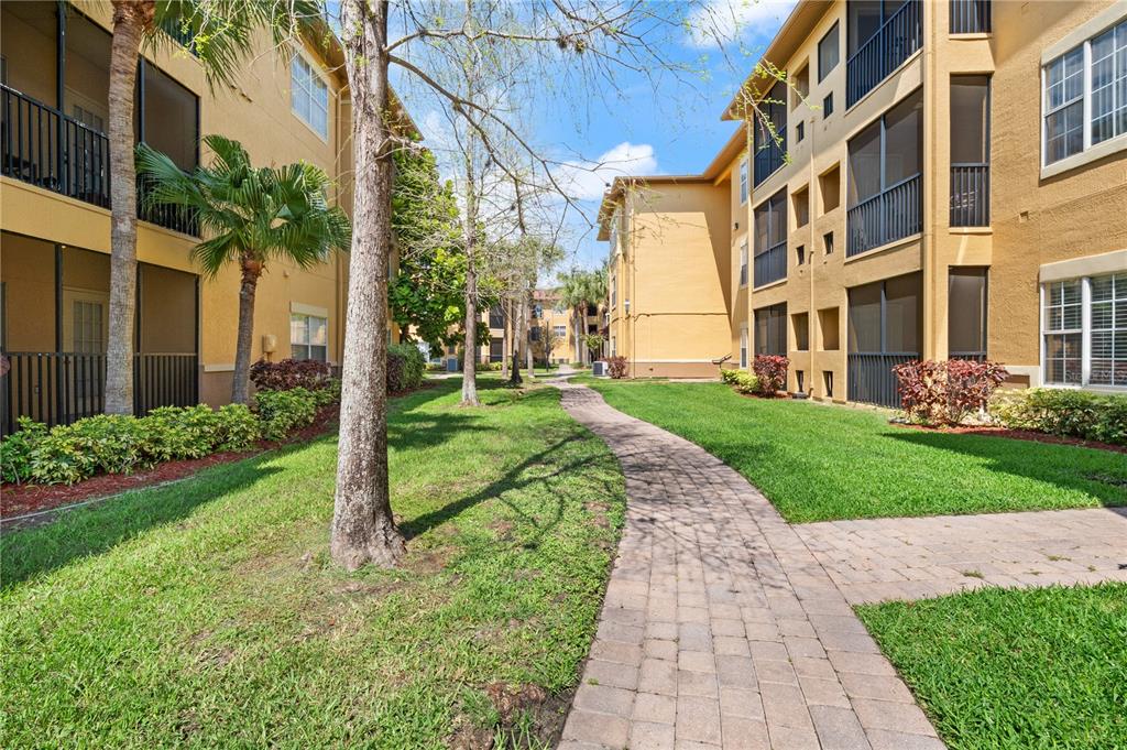 A paved walkway winds between two multi-story apartment buildings with screened balconies and green lawns — 4307 BAYSIDE VILLAGE DRIVE UNIT 103, TAMPA, FL