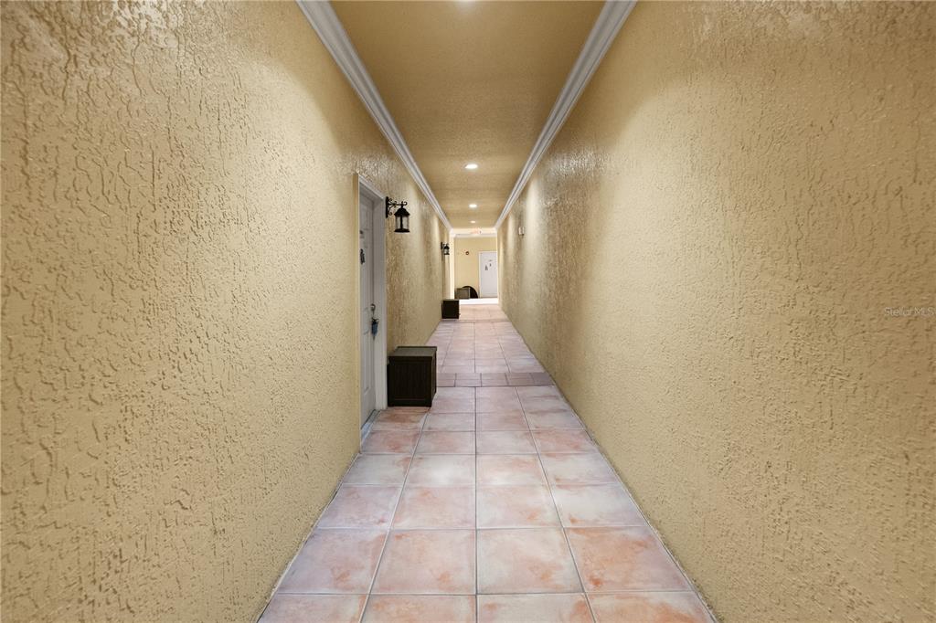 A long, narrow outdoor hallway features beige textured walls, tiled flooring, and recessed ceiling lights — 4307 BAYSIDE VILLAGE DRIVE UNIT 103, TAMPA, FL
