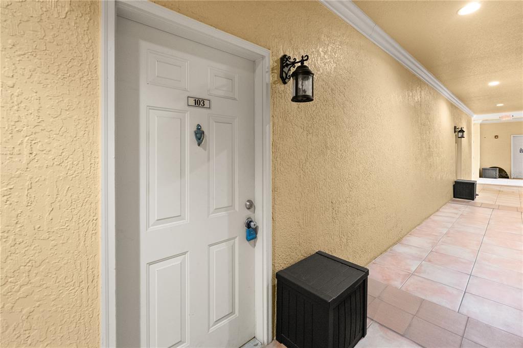 A white front door labeled 103 sits on a tiled outdoor walkway with yellow walls — 4307 BAYSIDE VILLAGE DRIVE UNIT 103, TAMPA, FL