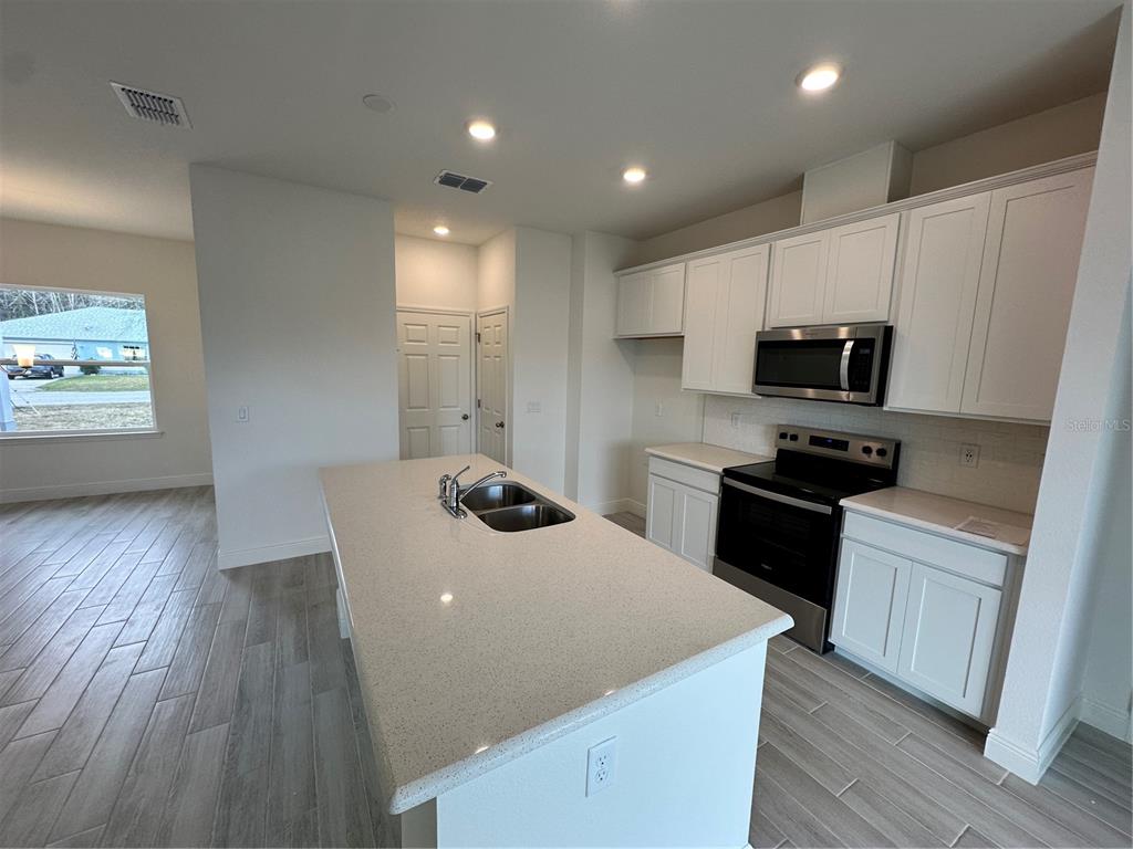 A modern kitchen features white cabinets, stainless steel appliances, a quartz island, and tile flooring — 14 LONDONDERRY DRIVE, PALM COAST, FL