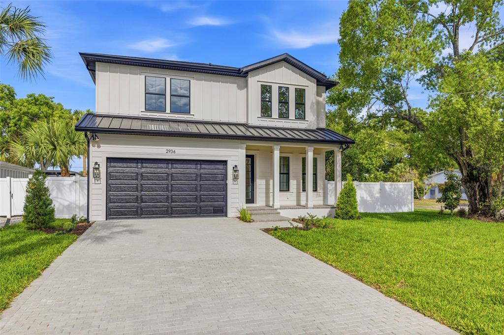 A two-story house with white vertical siding, a dark metal roof, and a paved driveway — 2936 W ROGERS AVENUE, TAMPA, FL