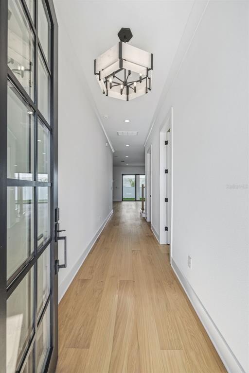 A long hallway with light wood flooring, white walls, and a modern hexagonal chandelier — 2936 W ROGERS AVENUE, TAMPA, FL