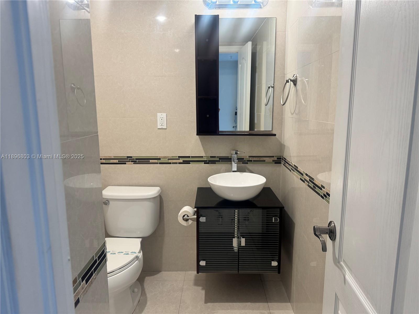 A small bathroom features a vessel sink, a dark vanity, and beige tiled walls — 19370 Collins Ave # 1520, Sunny Isles Beach FL 33160, SUNNY ISLES BEACH, FL