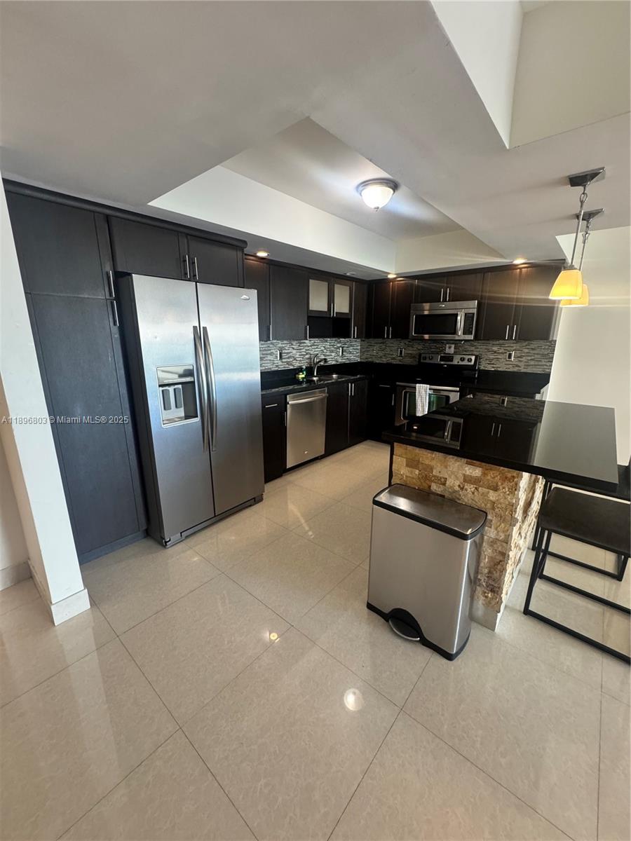A modern kitchen features dark cabinetry, stainless steel appliances, and a stone-accented breakfast bar — 19370 Collins Ave # 1520, Sunny Isles Beach FL 33160, SUNNY ISLES BEACH, FL