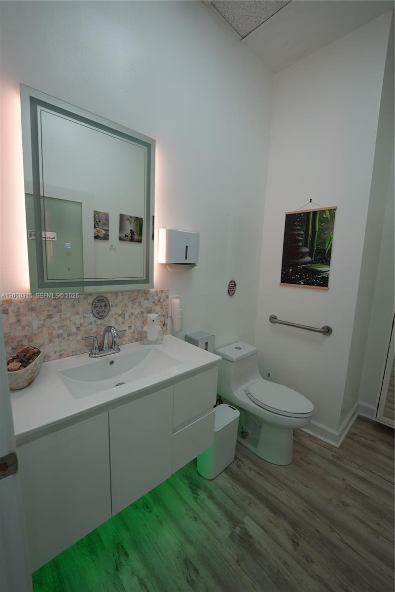 A modern bathroom features a white vanity, an illuminated mirror, and a toilet with grab bars — 7171 SW 24th St, Miami FL 33155, MIAMI, FL