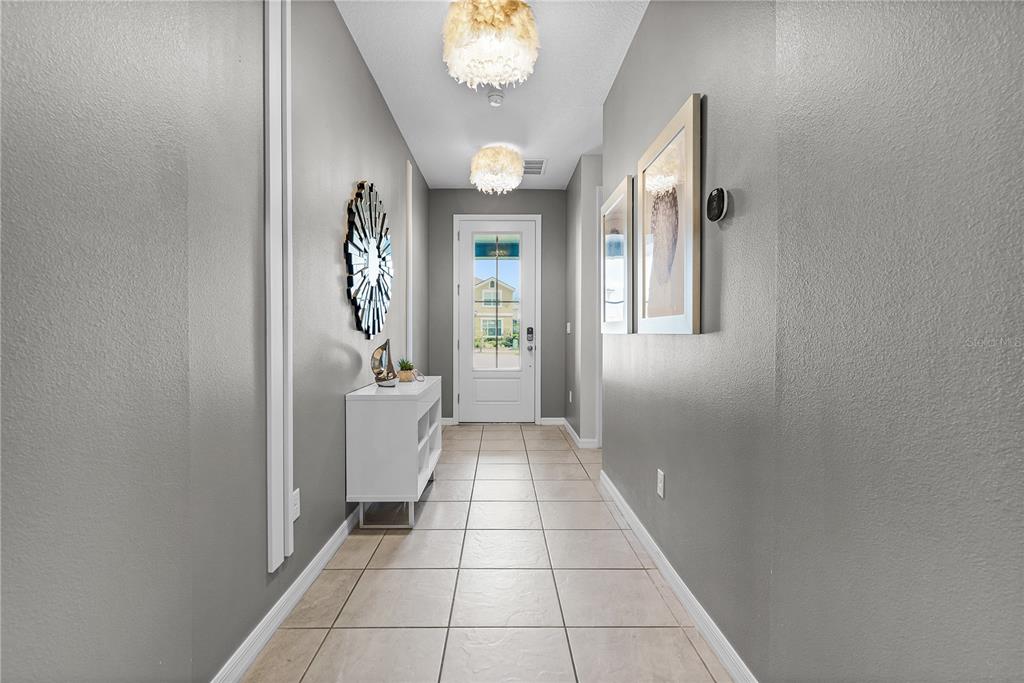 A hallway with gray walls, tile flooring, two light fixtures, and a white front door — 8915 TROPICAL HAVEN COURT, KISSIMMEE, FL