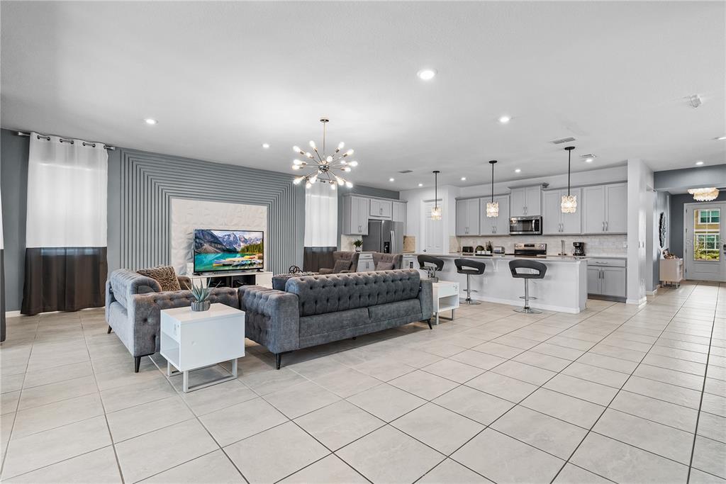 An open-concept living room and kitchen featuring gray cabinetry, tile flooring, and a tufted sofa — 8915 TROPICAL HAVEN COURT, KISSIMMEE, FL