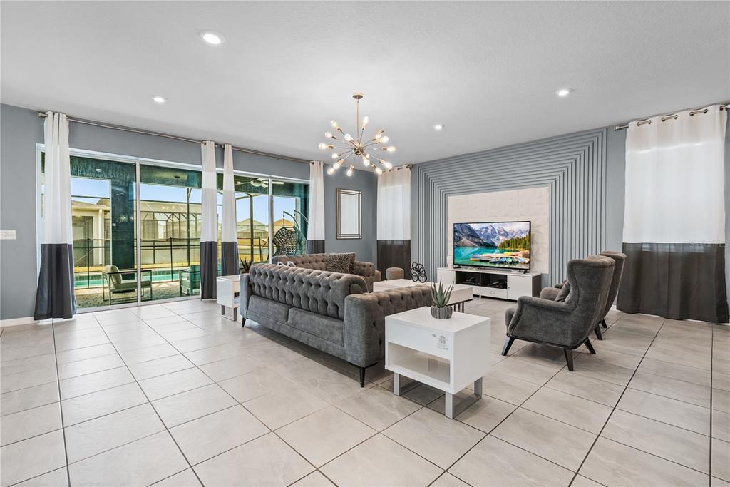 A living room features a tufted grey sofa, accent chairs, and a wall-mounted television — 8915 TROPICAL HAVEN COURT, KISSIMMEE, FL