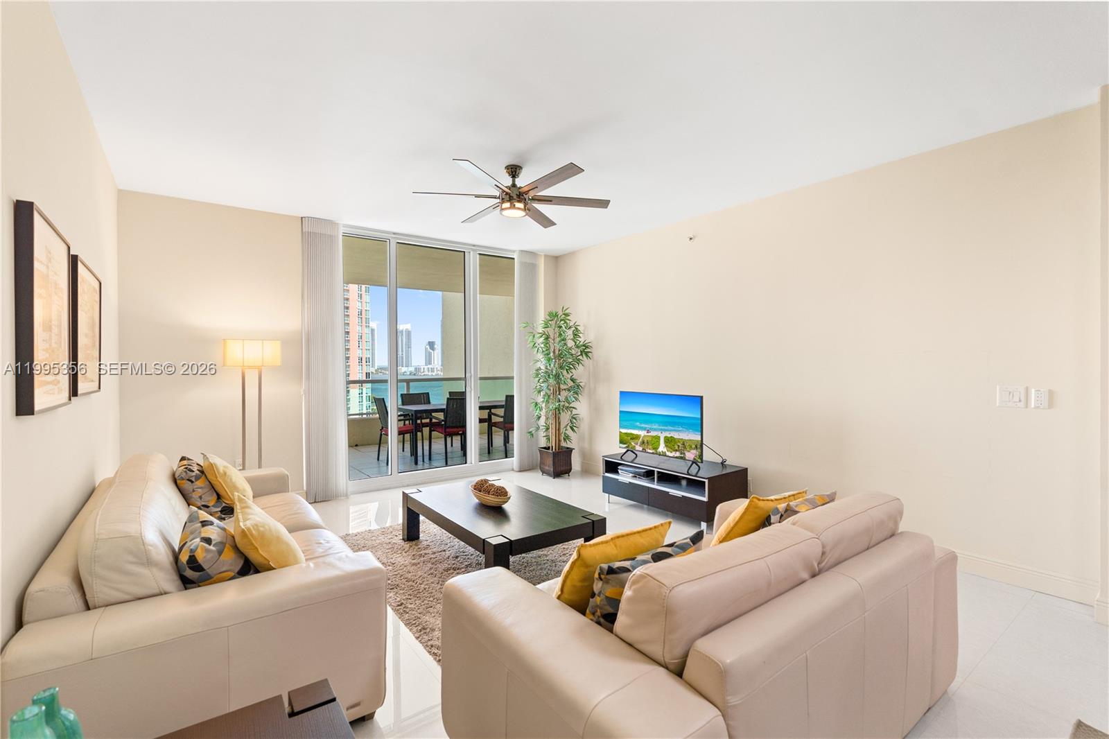 A living room features two beige sofas, a coffee table, and a balcony with water views — 3340 NE 190th St # 1004, Aventura FL 33180, AVENTURA, FL