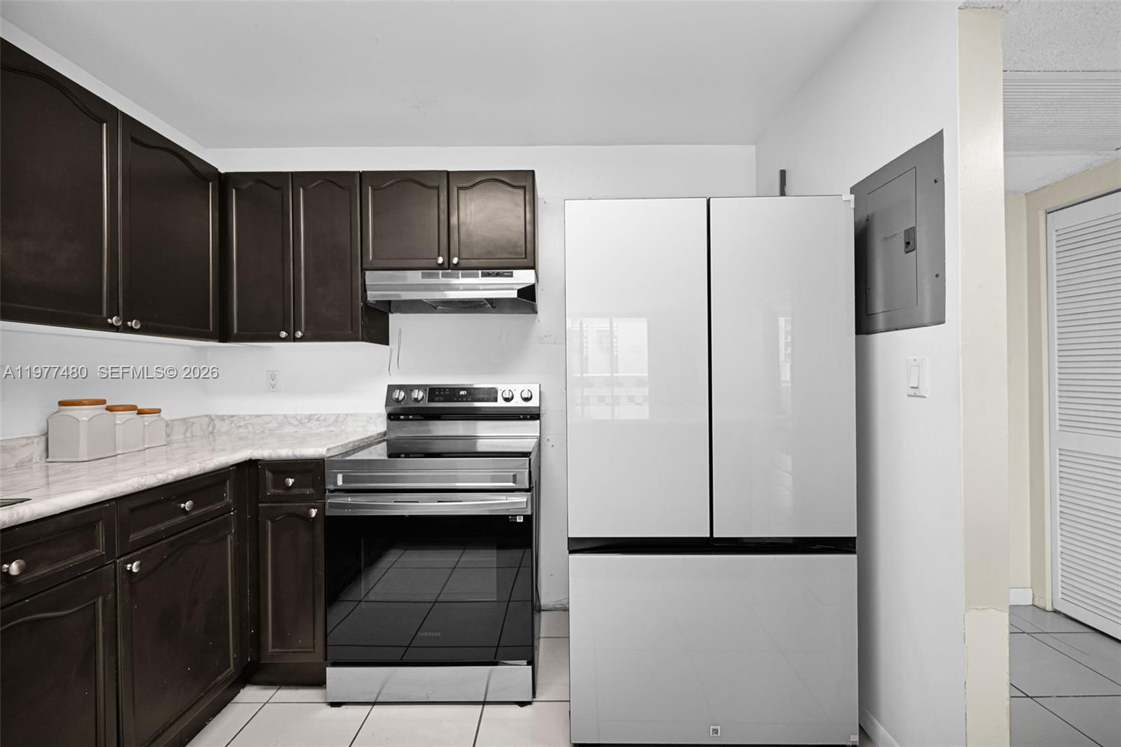 A kitchen features dark wood cabinets, a stainless steel stove, and a white refrigerator — 2301 Collins Ave # 802, Miami Beach FL 33139, MIAMI BEACH, FL