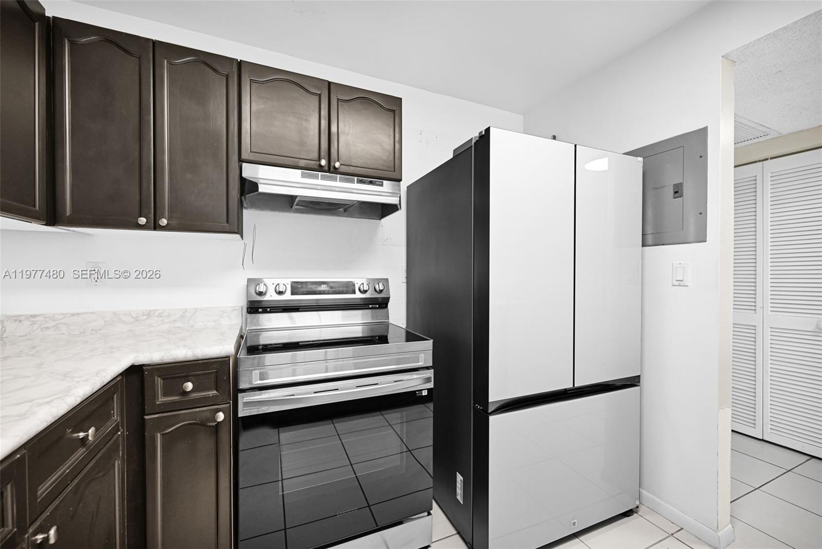 A kitchen features dark wood cabinets, a stainless steel stove, and a modern refrigerator — 2301 Collins Ave # 802, Miami Beach FL 33139, MIAMI BEACH, FL