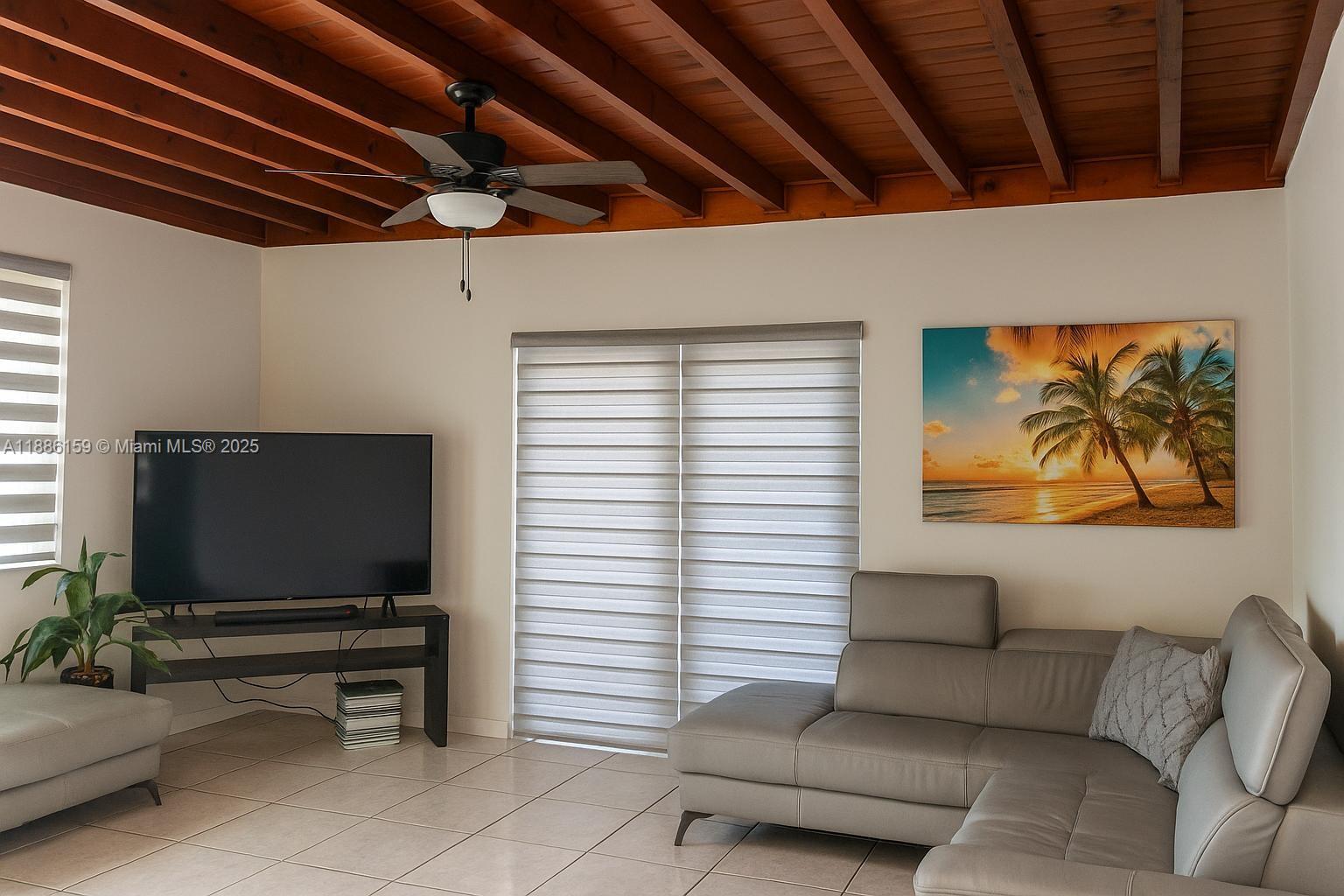 A living room features a grey sectional sofa, a television on a stand, and wood-beamed ceilings — 255 Central Blvd, Miami FL 33144, MIAMI, FL