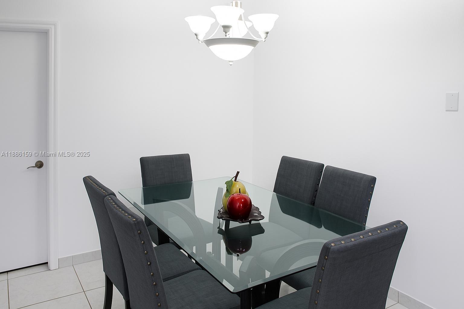 A dining area features a glass-topped table with six grey upholstered chairs and a chandelier — 255 Central Blvd, Miami FL 33144, MIAMI, FL
