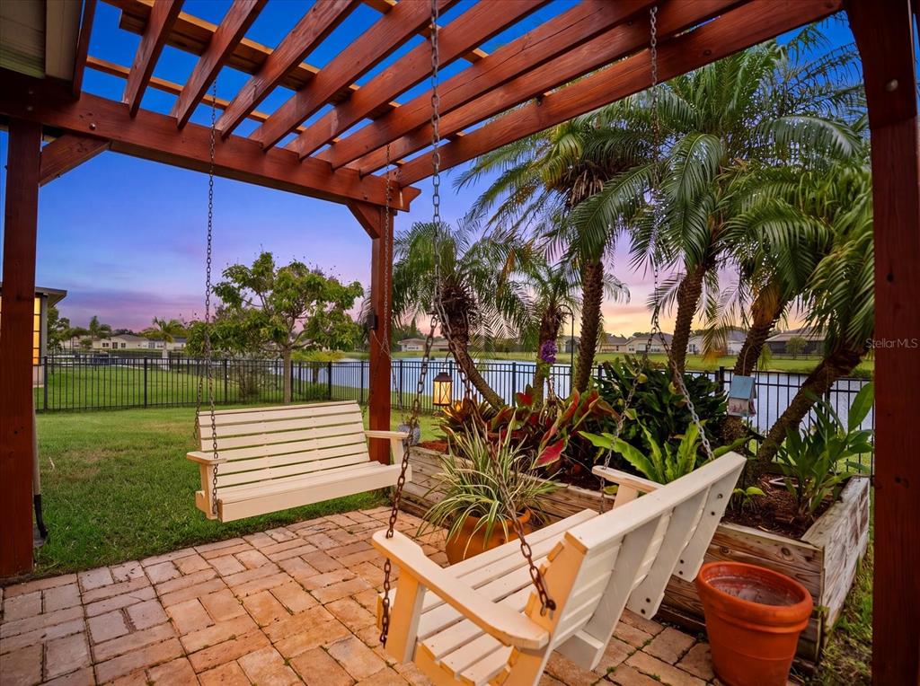 A patio with two white wooden swings under a pergola overlooking a lake and lawn — 5020 98TH AVENUE E, PARRISH, FL