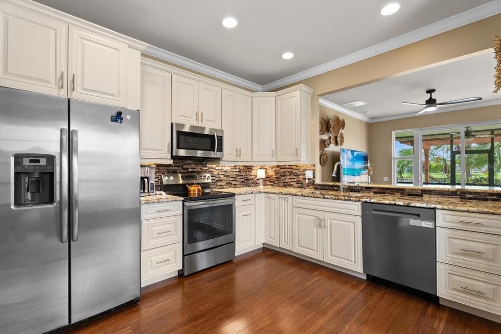 A kitchen features white cabinets, stainless steel appliances, granite countertops, and dark wood flooring — 5020 98TH AVENUE E, PARRISH, FL