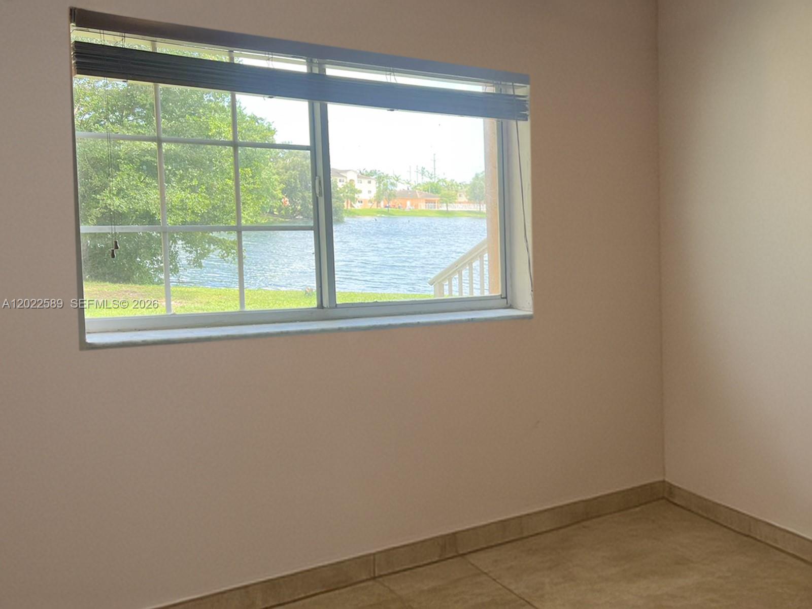 An empty room features tile flooring, plain walls, and a window overlooking a lake — 3690 N 56th Ave # 916, Hollywood FL 33021, HOLLYWOOD, FL