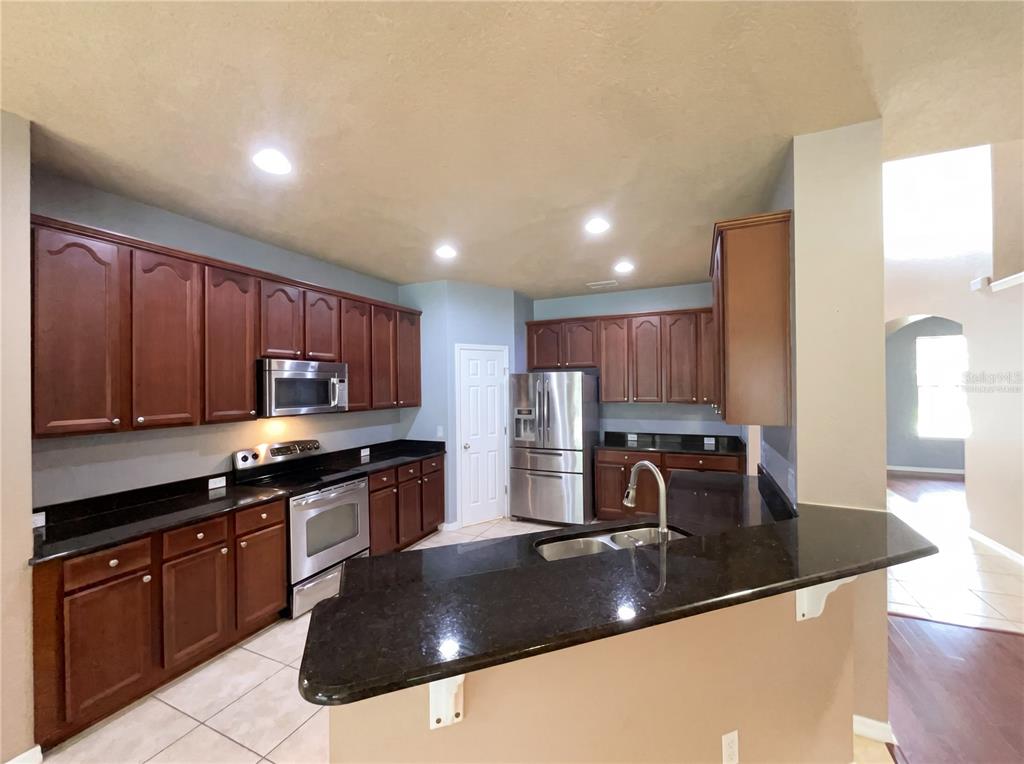 A kitchen features dark wood cabinets, black granite countertops, and stainless steel appliances — 15130 OVATION DRIVE, WINTER GARDEN, FL