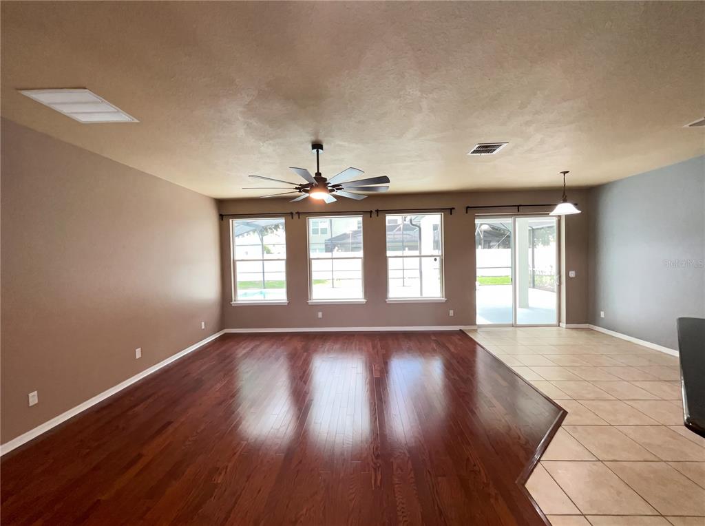 A living room with dark hardwood floors, tile flooring, a ceiling fan, and large windows — 15130 OVATION DRIVE, WINTER GARDEN, FL